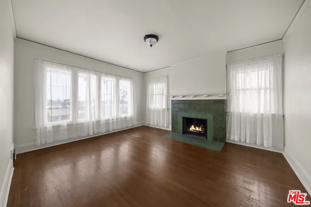 a view of an empty room with wooden floor fireplace and a window