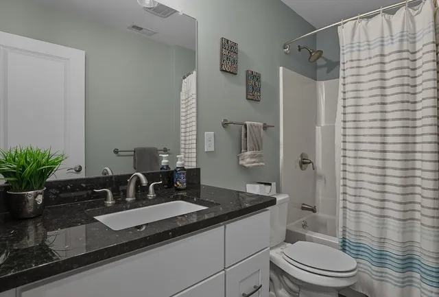 a bathroom with a granite countertop sink a toilet a mirror and shower