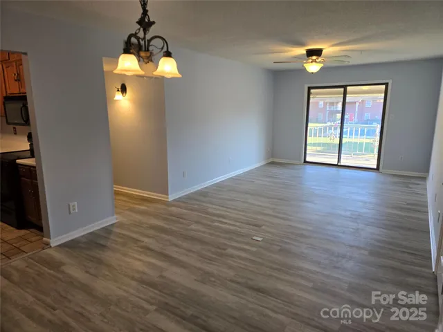 an empty room with wooden floor chandelier and windows