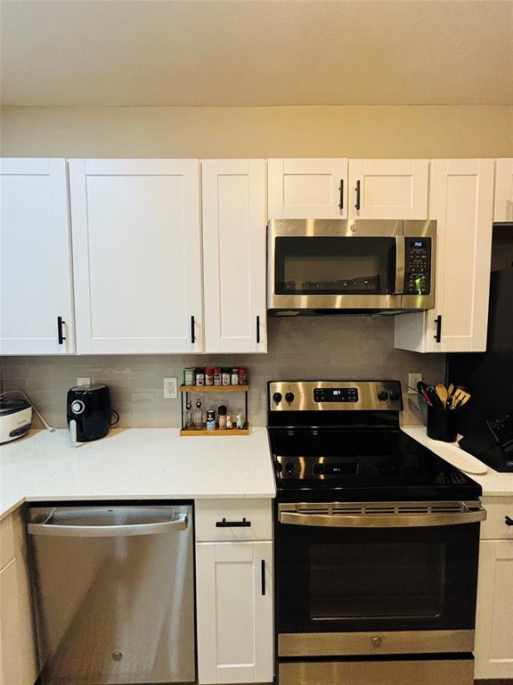 White shaker-style cabinetry, solid surface countertops, stainless steel appliances, and a tiled backsplash