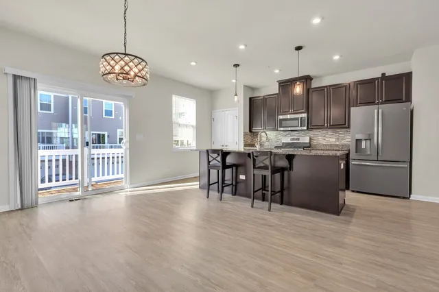 a open kitchen with stainless steel appliances granite countertop a stove top oven a refrigerator a dining table and chairs with wooden floor