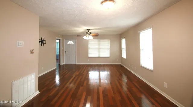 an empty room with wooden floor fan and windows