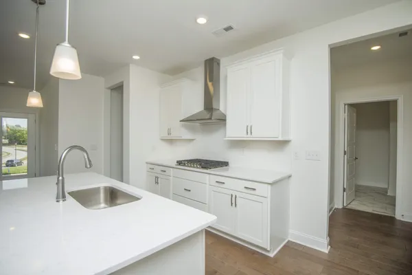 a large kitchen with granite countertop a large kitchen island a sink dishwasher a refrigerator and white cabinets with wooden floor