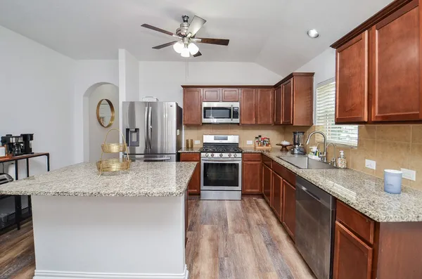 a kitchen with stainless steel appliances granite countertop a refrigerator a sink dishwasher a stove with wooden cabinets and floor