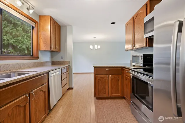 a kitchen with stainless steel appliances granite countertop a refrigerator a sink dishwasher a stove and white countertops with wooden floor