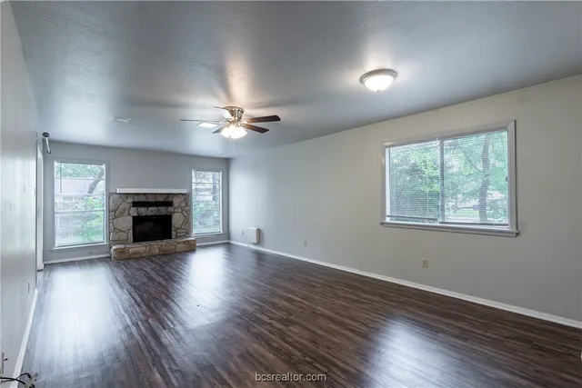 an empty room with wooden floor fireplace and windows