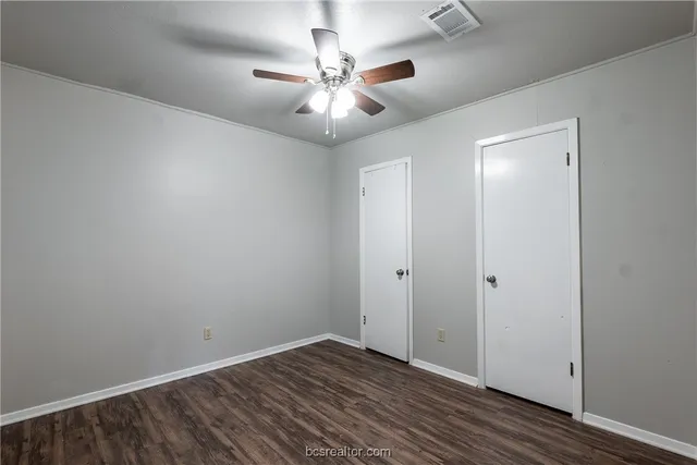an empty room with wooden floor and fan