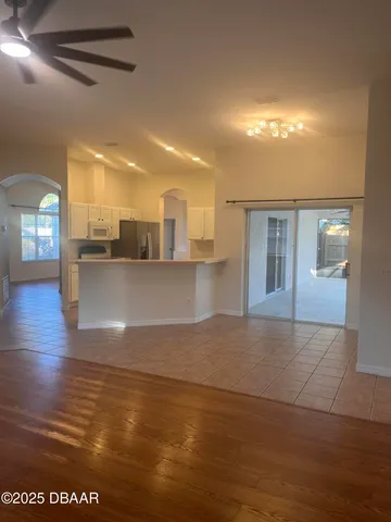 a view of a living room a kitchen with stainless steel appliances wooden floor and chandelier