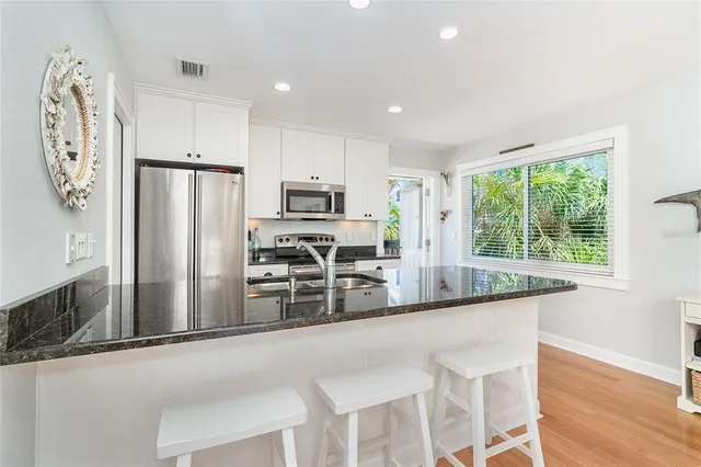 a kitchen with stainless steel appliances granite countertop a refrigerator a stove a sink and a dining table with wooden floor