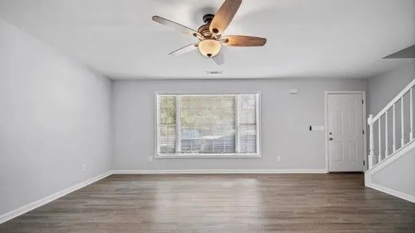 an empty room with wooden floor chandelier fan and windows