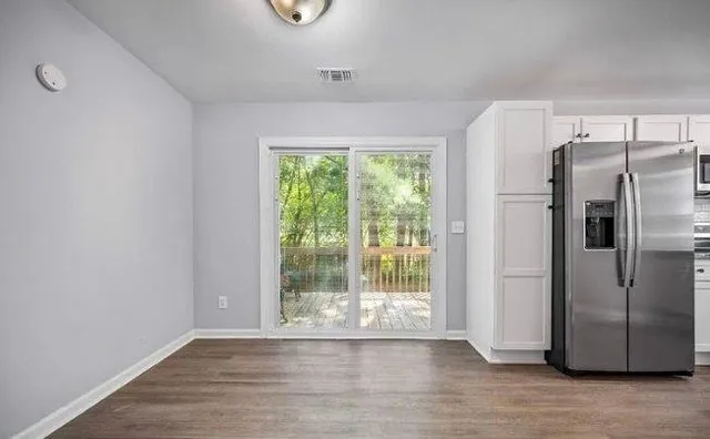 a view of a refrigerator in kitchen and an empty room with wooden floor