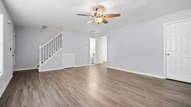 a view of an empty room with wooden floor and a ceiling fan
