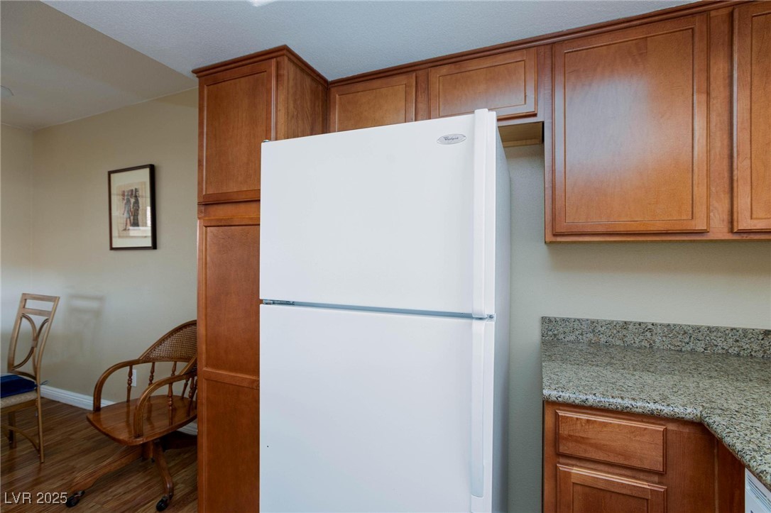 7300 West Pirates Cove Road, Unit 2038 Las Vegas, NV 89145 - Photo 8 of 26 Kitchen with freestanding refrigerator, brown cabinetry, light stone countertops, and dark wood finished floors
