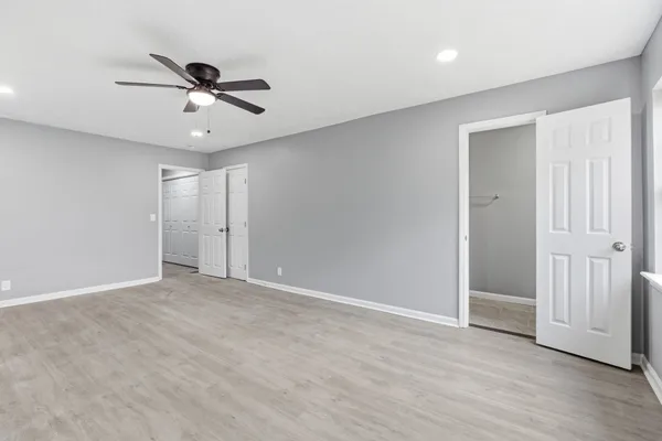 a view of an empty room with wooden floor and a ceiling fan