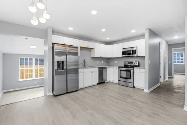 a kitchen with granite countertop a refrigerator oven a sink dishwasher and white cabinets with wooden floor