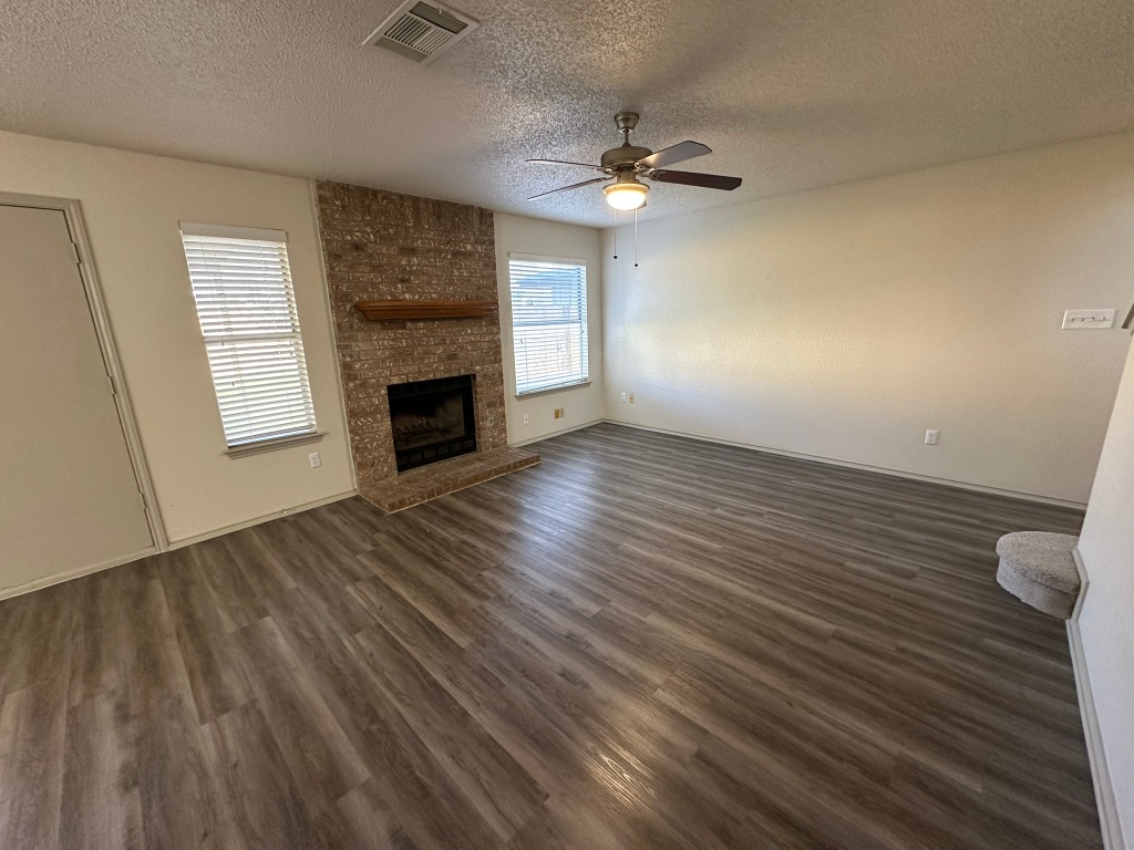 814 Smoke Signal Pass Pflugerville, TX 78660 - Photo 6 of 29 Unfurnished living room with a ceiling fan, a brick fireplace, and dark wood-style floors