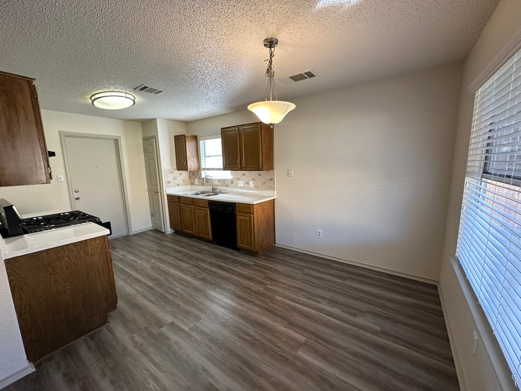 814 Smoke Signal Pass Pflugerville, TX 78660 - Photo 7 of 29 Kitchen featuring light countertops, a hanging light fixtures, dark wood-style floors, and black dishwasher