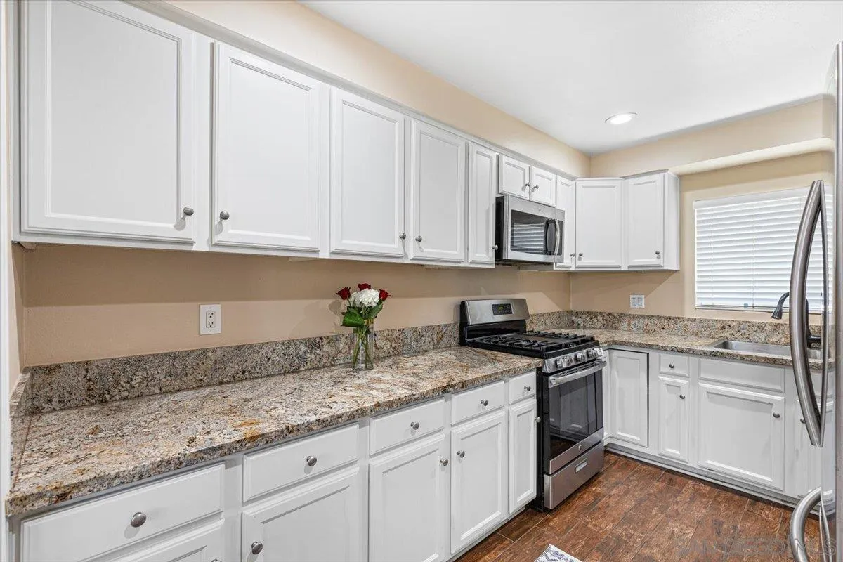 6295 Calle Pavana San Diego, CA 92139 - Photo 10 of 27 a kitchen with granite countertop white cabinets sink and stainless steel appliances