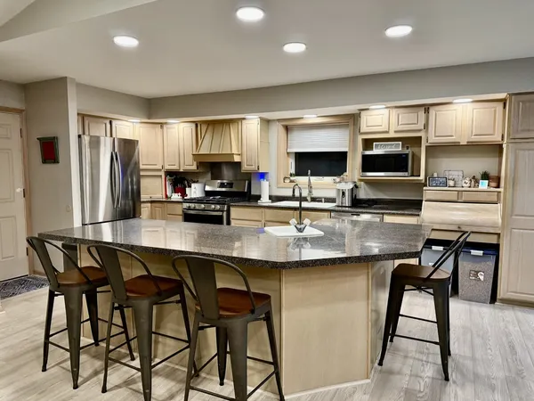 a kitchen with stainless steel appliances kitchen island granite countertop a dining table chairs refrigerator and sink
