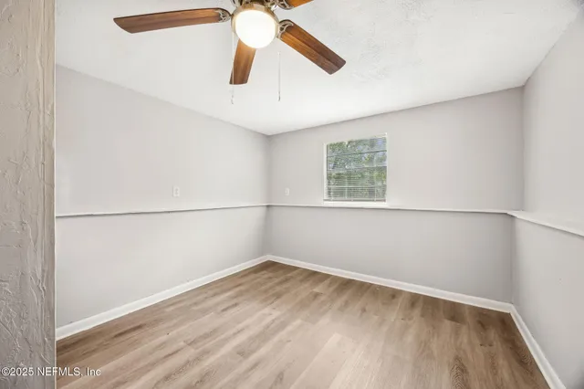an empty room with wooden floor fan and windows