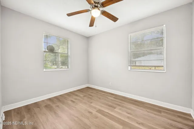 an empty room with wooden floor ceiling fan and windows