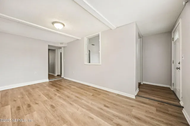 a view of an empty room with wooden floor and a window