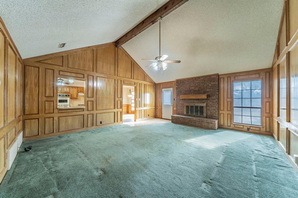 1202 Panorama Loop Waxahachie, TX 75165 - Photo 2 of 26 Unfurnished living room with a fireplace, a textured ceiling, carpet, wood walls, and a decorative wall