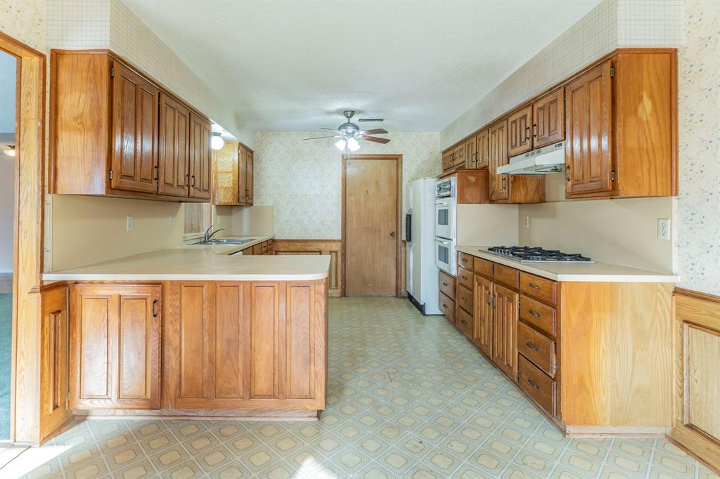 1202 Panorama Loop Waxahachie, TX 75165 - Photo 6 of 26 Kitchen featuring wallpapered walls, light flooring, light countertops, a peninsula, and brown cabinetry
