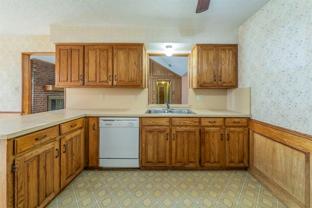 1202 Panorama Loop Waxahachie, TX 75165 - Photo 7 of 26 Kitchen with wallpapered walls, a wainscoted wall, brown cabinets, light floors, and white dishwasher