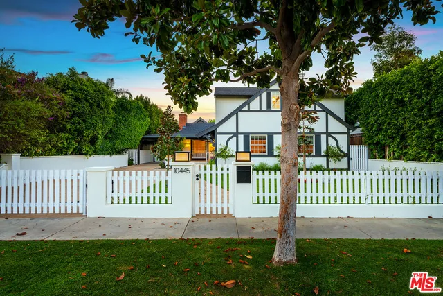 a view of a patio with couches table and chairs under an umbrella with plants and trees