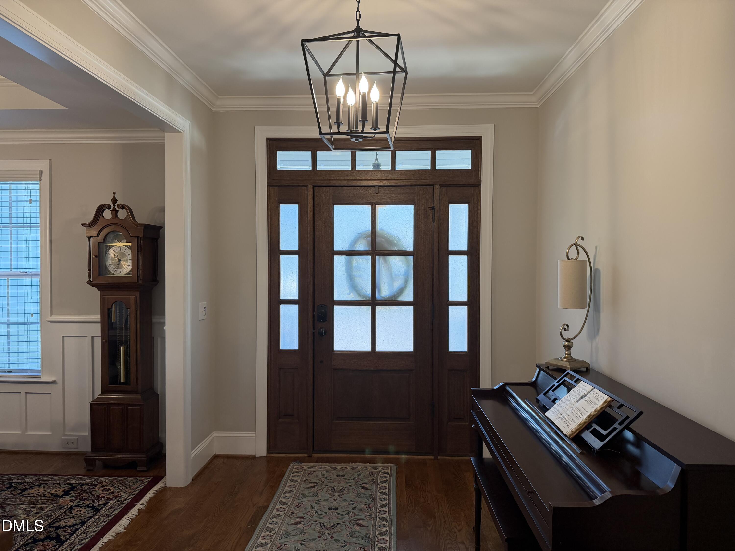 1404 Ivy Lane Raleigh, NC 27609 - Photo 4 of 37 Wood-finish flooring, crown molding, and a solid wood entry door with transom window and sidelights, complemented by a geometric pendant light fixture