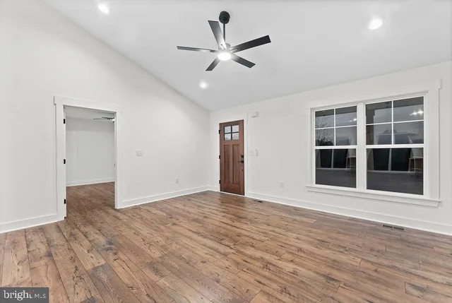 a view of an empty room with wooden floor and a ceiling fan