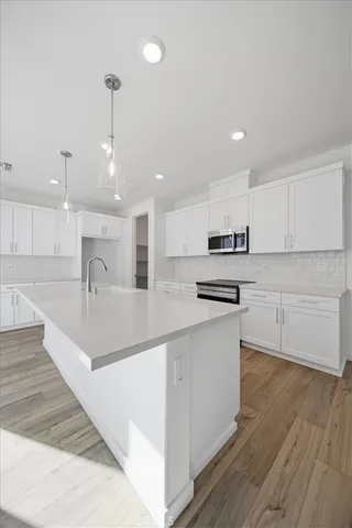 a large white kitchen with wooden floor and stainless steel appliances