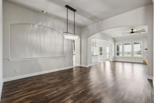 an empty room with wooden floor a ceiling fan and windows