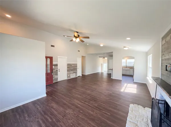 a view of an empty room with wooden floor and a kitchen
