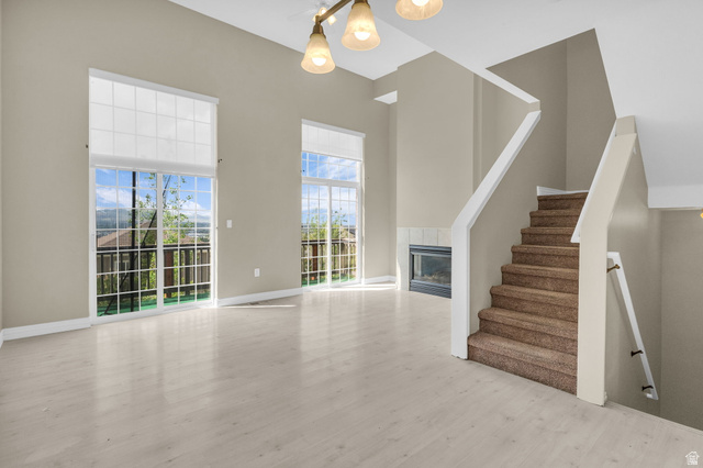 14108 Pepi Band Road Draper, UT 84020 - Photo 4 of 36 Spacious room featuring vaulted ceilings, light wood-finish flooring, two large sliding glass doors with upper windows, and a built-in fireplace with a tiled surround