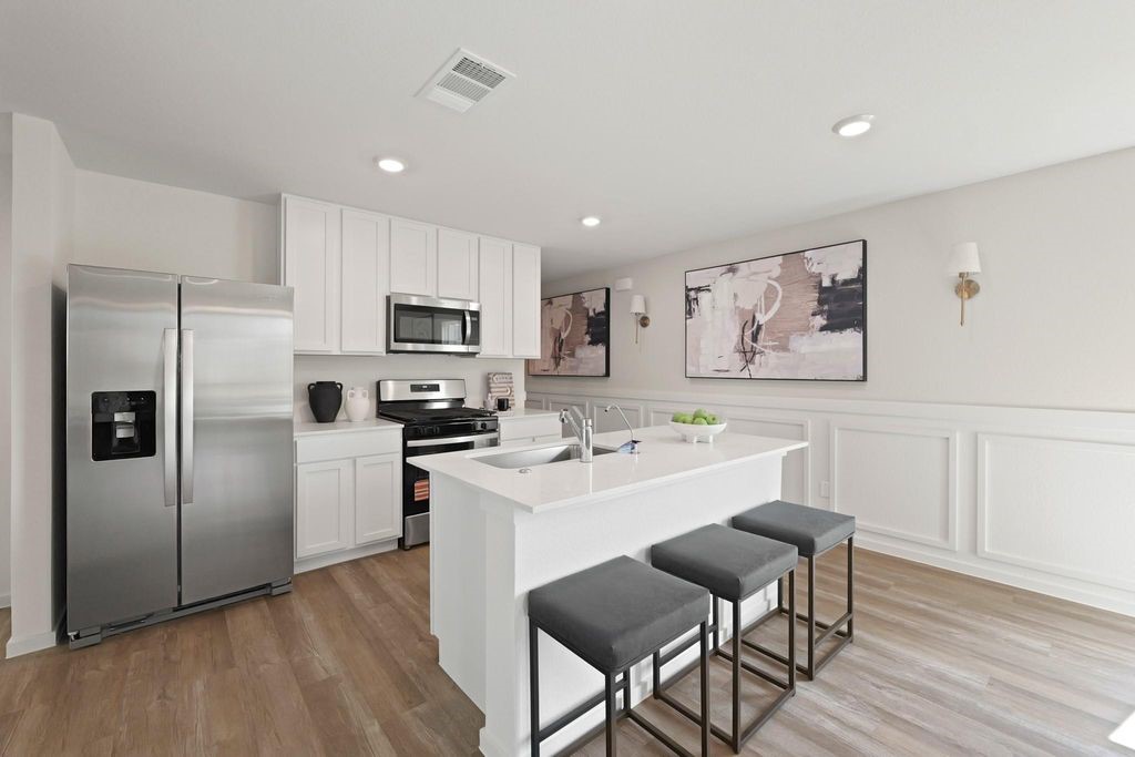 24114 Chirp Street Splendora, TX 77372 - Photo 4 of 22 a kitchen with a refrigerator a stove a microwave oven a sink a dining table and chairs with wooden floor