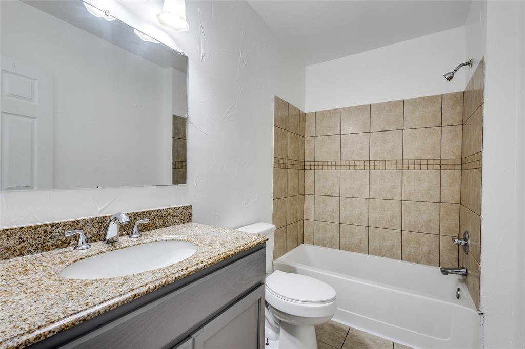 618 East Woodard Street Denison, TX 75021 - Photo 17 of 22 a bathroom with a granite countertop sink a toilet a mirror a bathtub and shower