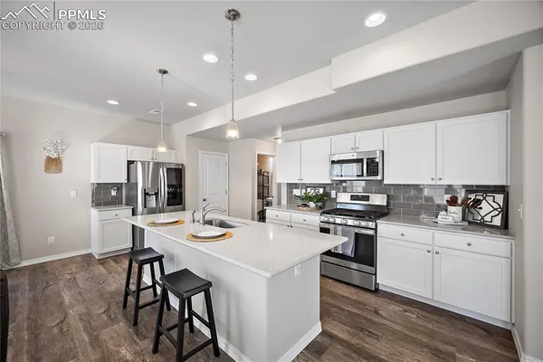 a kitchen with stainless steel appliances kitchen island granite countertop a stove a sink a refrigerator and white cabinets with wooden floor