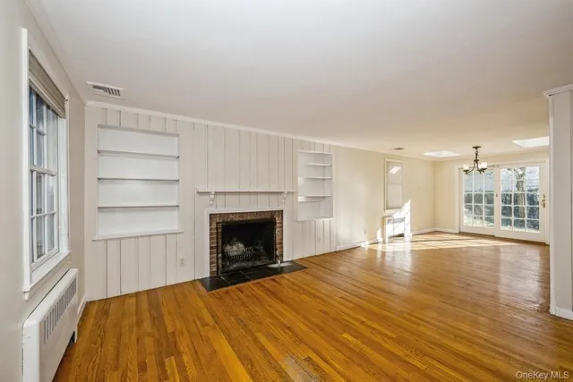 a view of an empty room with wooden floor fireplace and a window