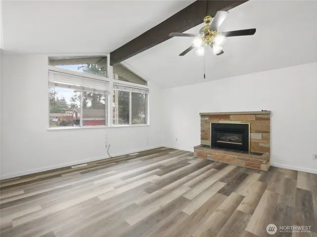 a view of an empty room with wooden floor fireplace and a window