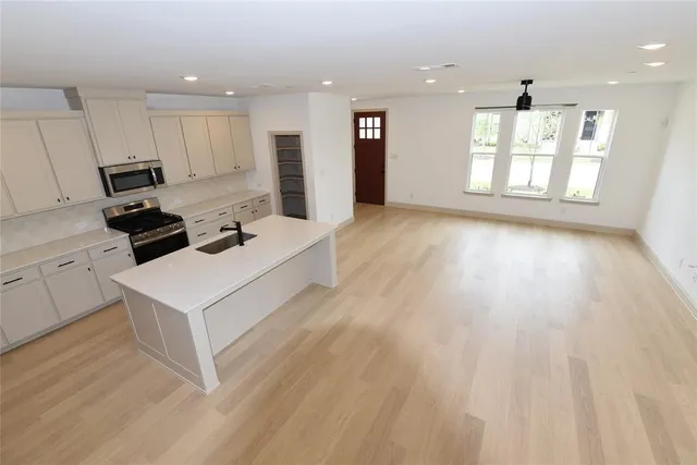 a living room with stainless steel appliances kitchen island hardwood floor and a window