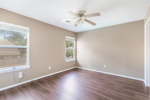 an empty room with wooden floor fan and windows