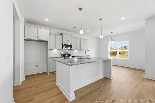 a kitchen with stainless steel appliances granite countertop a sink a stove a refrigerator and white cabinets with wooden floor