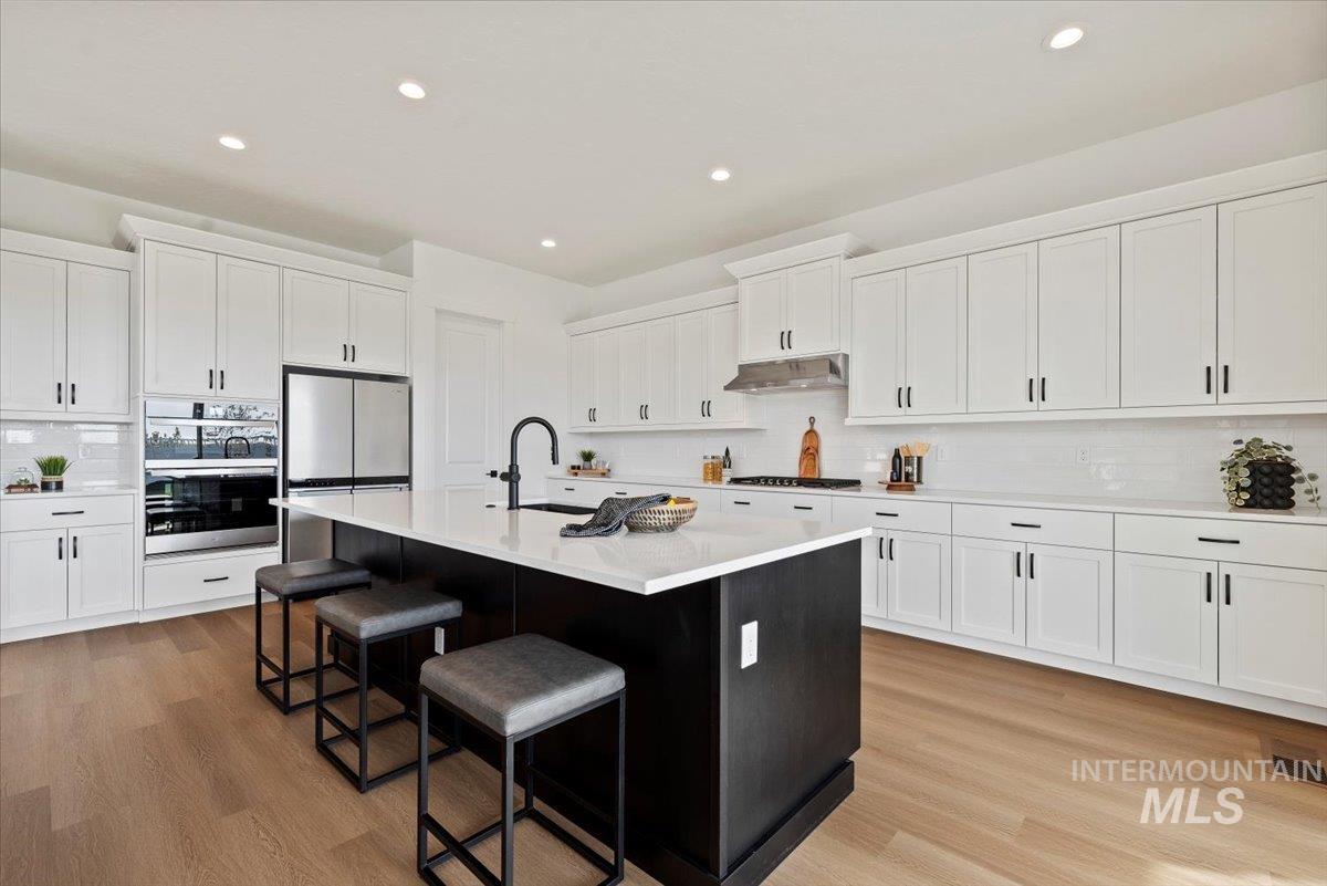 14701 Port Royal Street Caldwell, ID 83607 - Photo 11 of 40 Kitchen featuring decorative backsplash, white cabinets, appliances with stainless steel finishes, a center island with sink, and recessed lighting