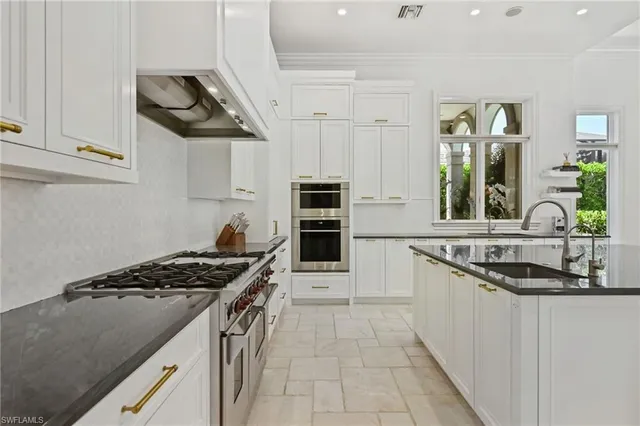 a view of a kitchen with kitchen island a large window cabinets a sink and stainless steel appliances
