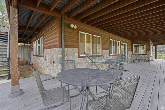 6 Beaver Springs Rancheros Oakley, UT 84055 - Photo 47 of 68 Expansive covered deck featuring wood-finish flooring, a stone foundation, a log-style exterior, multiple windows, and exposed ceiling beams