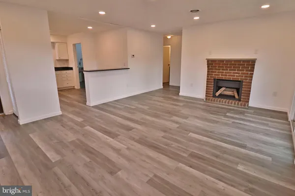 a view of empty room with wooden floor and kitchen