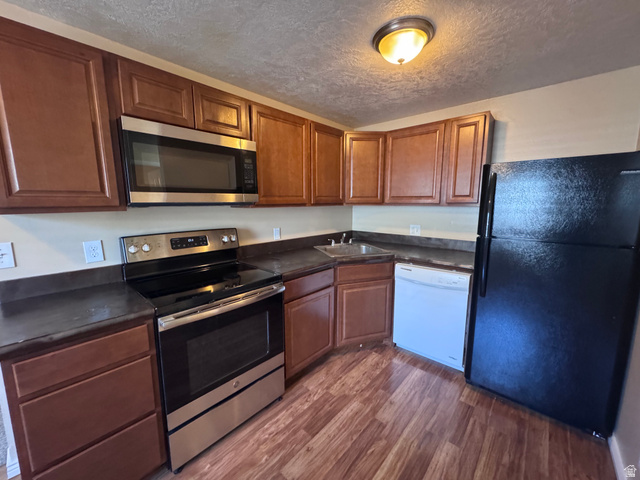 2182 West 5600th Street South Roy, UT 84067 - Photo 1 of 11 Kitchen featuring wood-finish flooring, dark countertops, and warm-toned cabinetry