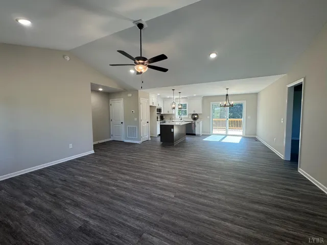 a view of an empty room and kitchen view with wooden floor